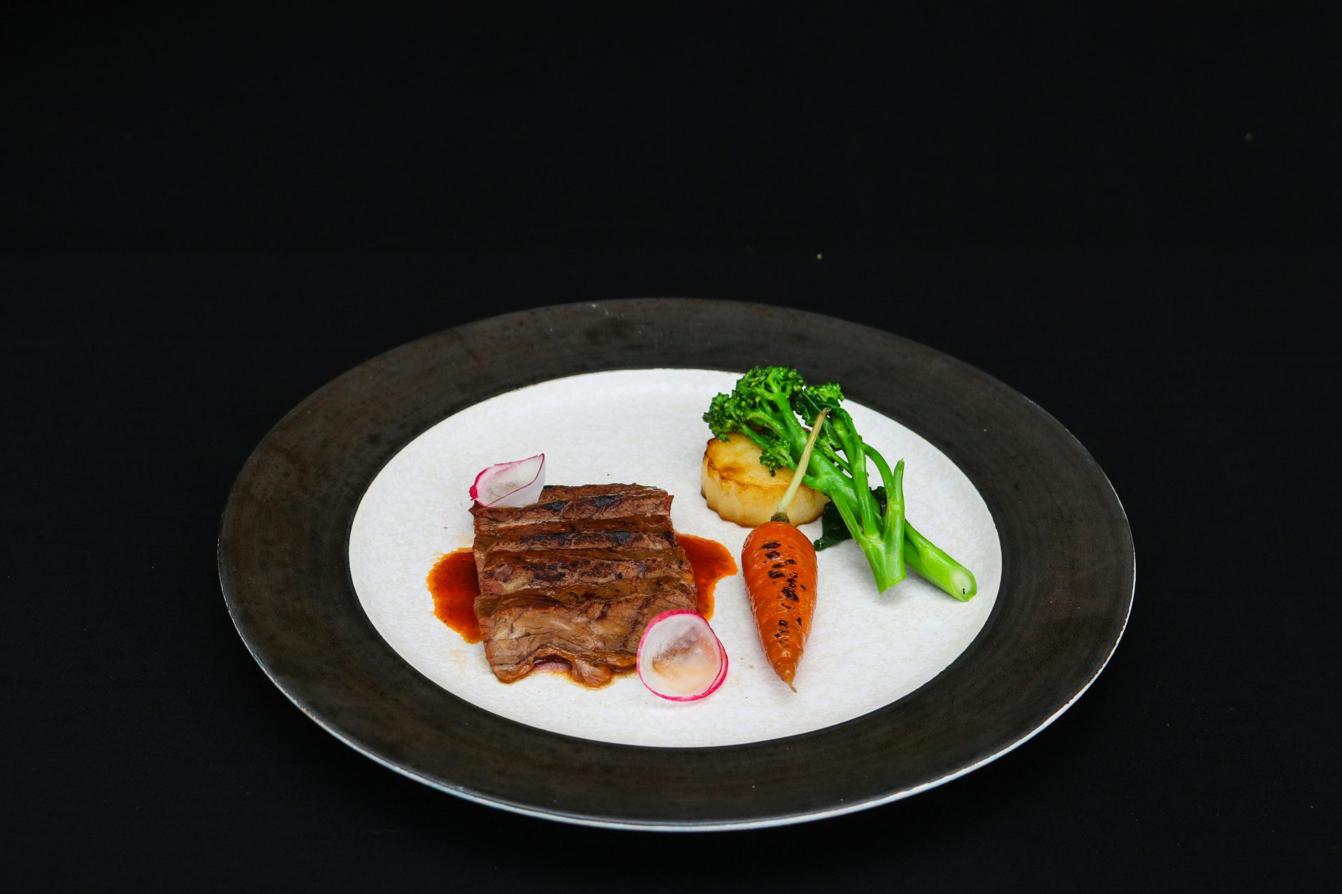 Un délicieux steak gourmet servi avec des légumes et une sauce dans une assiette élégante. Parfait pour les présentations culinaires.